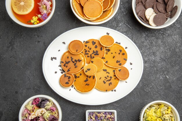 Draufsicht leckere Pfannkuchen mit Tee und Keksen auf dem dunklen Hintergrund