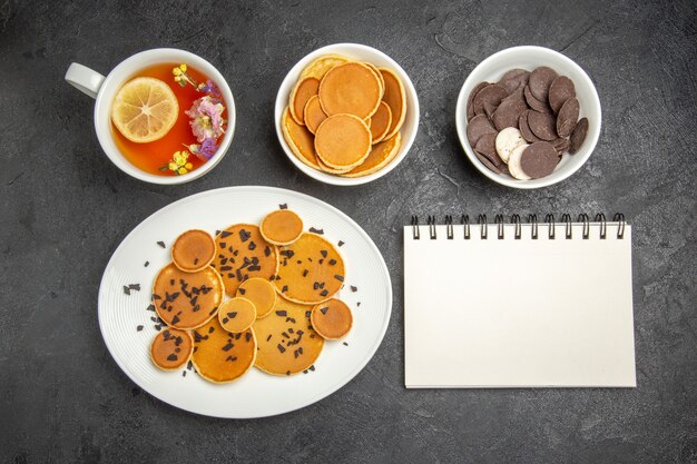 Draufsicht leckere Pfannkuchen mit Tee und Keksen auf dunklem Boden süßer Kuchen Dessertkuchen