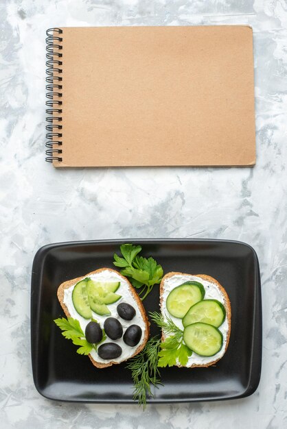 Draufsicht leckere Sandwiches mit Gurken und Oliven innerhalb der weißen Oberfläche der Platte