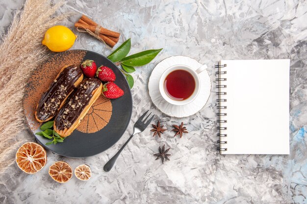 Draufsicht leckere Schoko-Eclairs mit Tasse Tee auf weißem Kekskuchen-Dessert-Keks