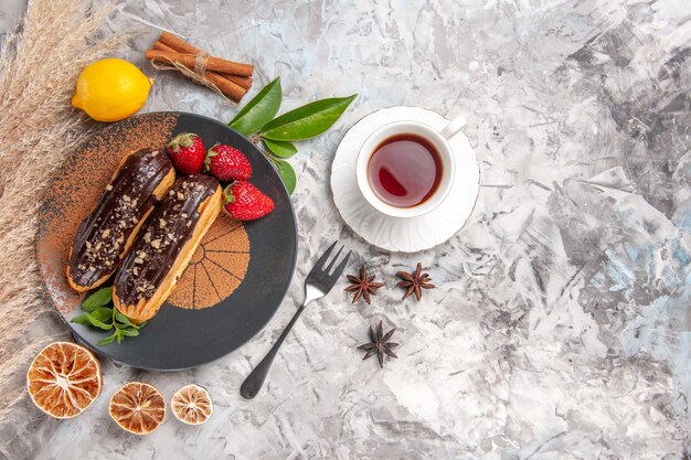 Draufsicht leckere Schoko-Eclairs mit Tasse Tee auf weißem Kekskuchen-Dessert-Keks