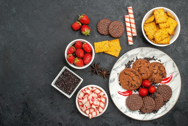 Draufsicht leckere Schoko-Kekse mit verschiedenen Snacks auf süßem Kekstee des dunklen Hintergrunds