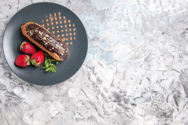 Draufsicht leckere Schokoladen-Eclairs mit Erdbeeren auf hellem Schreibtisch Dessertkuchen Obst