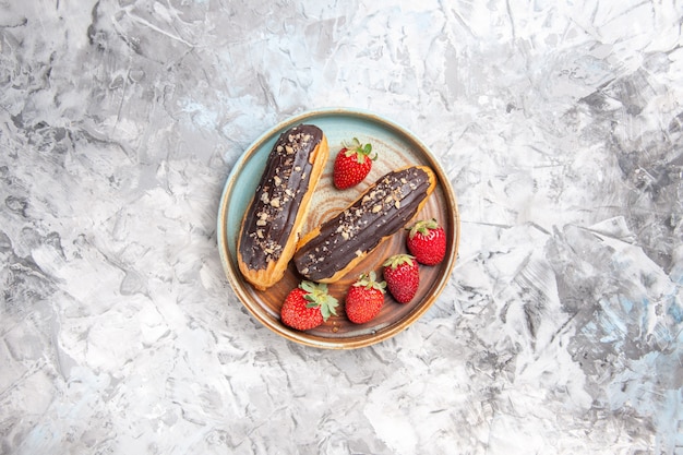 Draufsicht leckere schokoladen-eclairs mit erdbeeren auf leichten dessertkuchenfrüchten