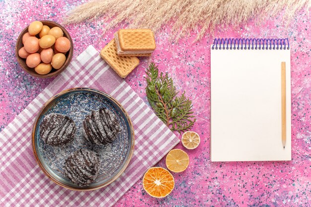 Draufsicht leckere Schokoladenkuchen mit Bonbons und Waffeln auf rosa