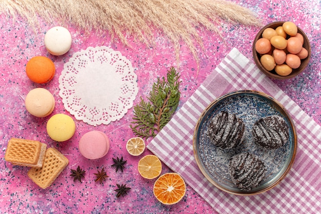 Draufsicht leckere Schokoladenkuchen mit Macarons und Waffeln auf rosa