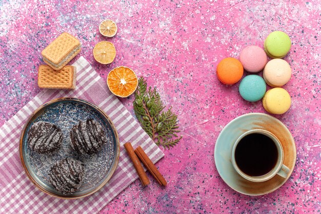 Draufsicht leckere Schokoladenkuchen mit Tasse Tee und französischen Macarons auf rosa