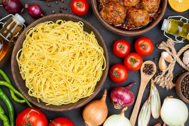 Draufsicht leckere Spaghetti in Schüssel Frikadellensuppe in Schüssel Ölflasche Zwiebeln Tomaten lange grüne Peperoni auf dem Tisch