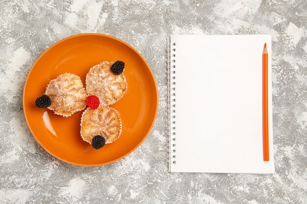 Draufsicht leckere Teigkuchen mit Zuckerpulver und Notizblock auf weißem Hintergrund