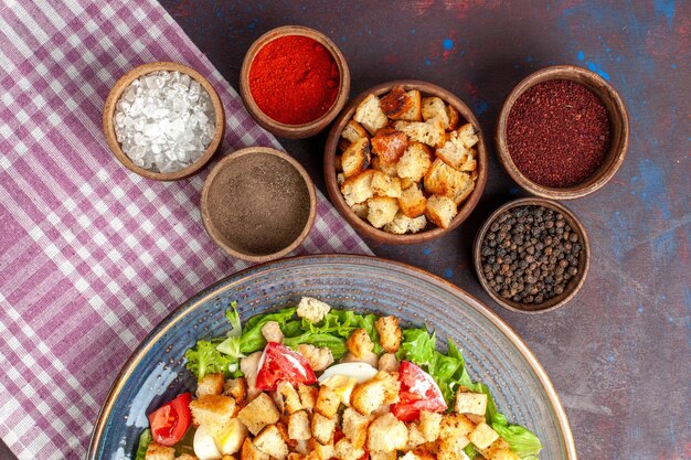 Draufsicht leckeren Caesar-Salat mit kleinen Zwieback und Gewürzen auf dem dunklen Schreibtisch