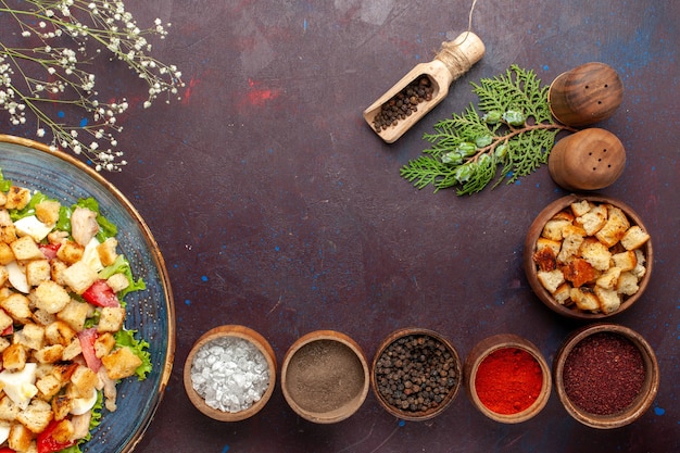 Draufsicht leckeren Caesar Salat mit verschiedenen Gewürzen auf der dunklen Oberfläche