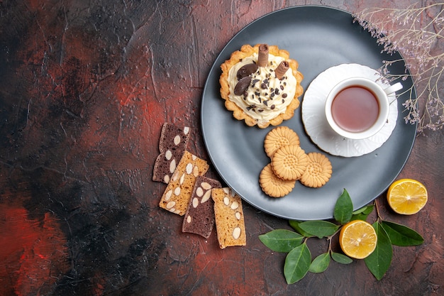 Draufsicht leckeren cremigen Kuchen mit Tee und Keksen auf dem dunklen Tisch süßer Kuchen Nachtisch