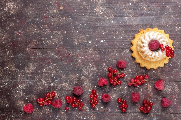 Draufsicht leckeren kleinen Kuchen mit Zuckerpulver zusammen mit Himbeeren Preiselbeeren alle entlang brauner rustikaler Hintergrund Beerenfruchtkuchen Keksfarbe