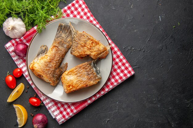 Draufsicht leckerer Fisch braten auf grauem Teller auf Serviette Dill Zitronenscheiben Kirschtomaten Knoblauch auf dunklem Hintergrund