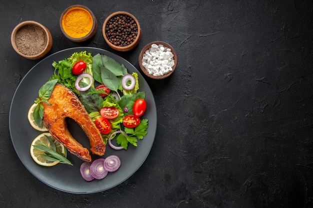 Draufsicht leckerer gekochter Fisch mit frischem Gemüse und Gewürzen auf dem dunklen Tisch