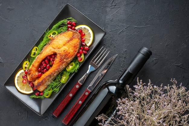 Draufsicht leckerer gekochter Fisch mit Gemüse und Zitronenscheiben in der Pfanne auf dunklem Tisch