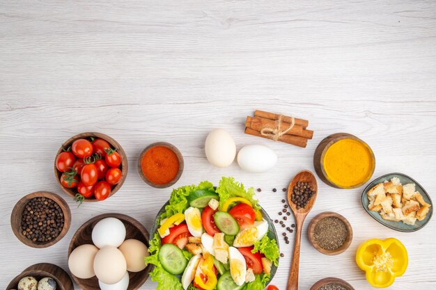 Draufsicht leckerer Gemüsesalat mit Eiergewürzen und Tomaten auf weißem Hintergrund Farbe reife Salatmahlzeit Essen Frühstück Mittagessen