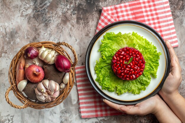 Draufsicht leckerer Granatapfelsalat auf grünem Salat mit Korb voller Gemüse auf hellem Hintergrund