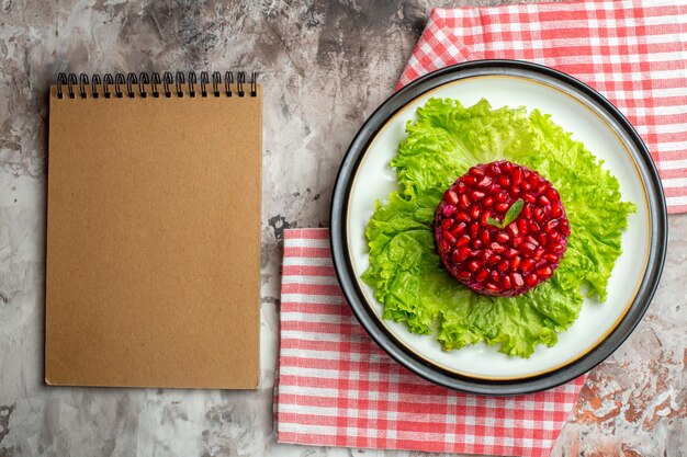 Draufsicht leckerer Granatapfelsalat rund auf grünem Salat auf hellem Hintergrund