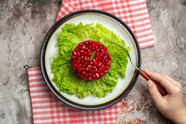 Draufsicht leckerer Granatapfelsalat rund auf grünem Salat auf hellem Hintergrund