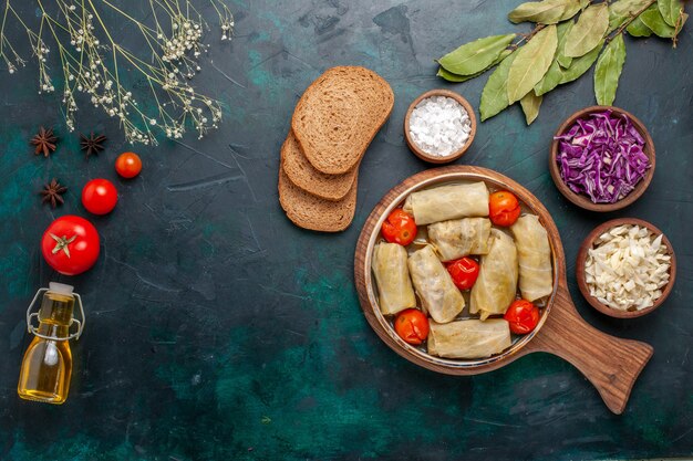 Draufsicht leckeres Fleischmehl gerollt mit Kohl und Tomaten genannt Dolma mit Öl und Brot auf dunkelblau