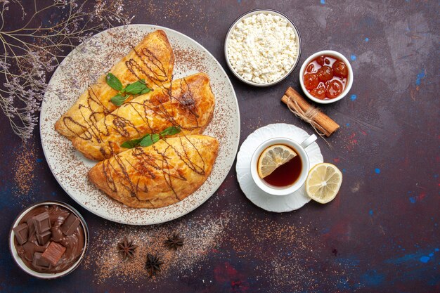 Draufsicht leckeres Gebäck mit Tasse Tee und Hüttenkäse auf dunklem Schreibtischgebäck süß backen Tee Kuchen Zuckerkeks