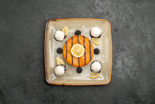 Draufsicht leckeres Kuchendessert mit Zitronenscheiben und Kokosbonbons auf einer dunklen Oberfläche Desserttee süße Kuchenkuchensüßigkeit