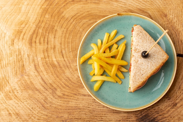 Kostenloses Foto draufsicht leckeres sandwich mit olivenschinken tomaten gemüse in platte mit pommes frites auf dem hölzernen hintergrund sandwich food snack frühstück