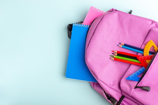 Draufsicht lila Tasche mit Heften und Stiften auf blauem Schreibtisch