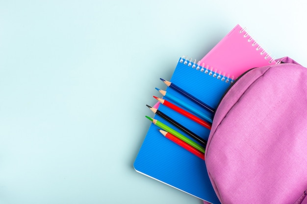 Draufsicht lila Tasche mit Heften und Stiften auf blauer Oberfläche