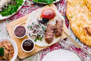 Kostenloses Foto draufsicht lula kebab auf fladenbrot mit zwiebeltomaten und saucen auf dem brett