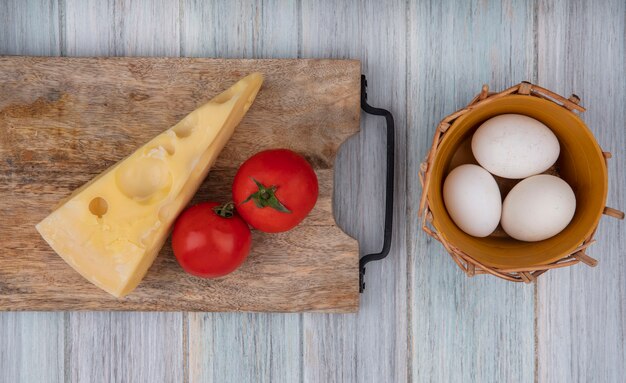 Draufsicht maasdam Käse mit Tomaten auf einem Stand und Hühnereiern zu einem Korb auf einem grauen Hintergrund