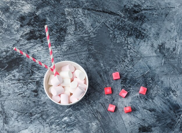 Draufsicht Marshmallows mit Zuckerrohr und roten Bonbons auf dunkelblauer Marmoroberfläche. horizontal
