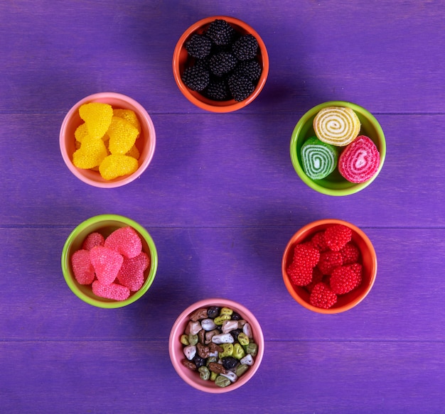 Draufsicht mehrfarbige Marmelade in verschiedenen Formen mit Pralinen in Form eines Steins in Untertassen für Marmelade auf lila Hintergrund