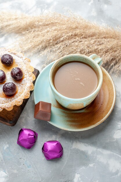 Draufsicht Milchkaffee mit Kirschkuchen und Bonbons auf dem hellen Tischkuchenkeks süßer Zuckerauflauf