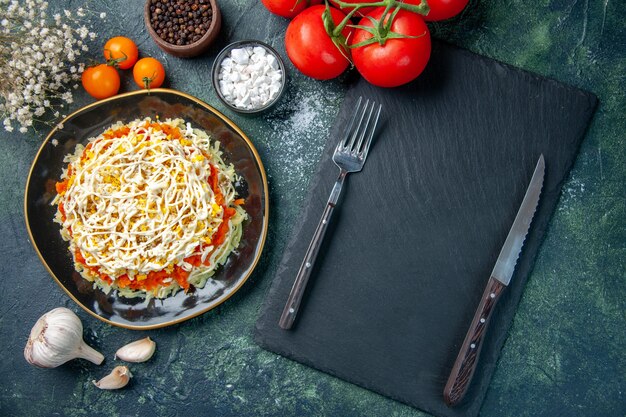 Draufsicht Mimosensalat innerhalb Platte mit Gewürzen und roten Tomaten auf dunkelblauem Hintergrund