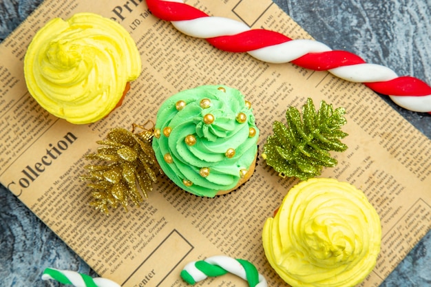 Draufsicht Mini Cupcakes Weihnachtsschmuck Bonbons auf Zeitung auf dunkler Oberfläche