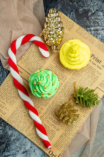Draufsicht Mini Cupcakes Weihnachtssüßigkeiten Weihnachtsornamente auf Zeitungs beige Schal auf dunkler Oberfläche