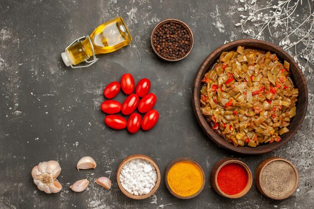 Draufsicht mit grünen Bohnen Teller mit grünen Bohnen mit Tomaten neben der Knoblauch-Tomaten-Flasche mit Ölschüssel mit Gewürzen auf dem dunklen Tisch