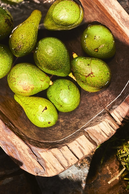 Draufsicht Nahaufnahme von grünen und gelben Avocados unter strömendem Wasser in einem Holztank