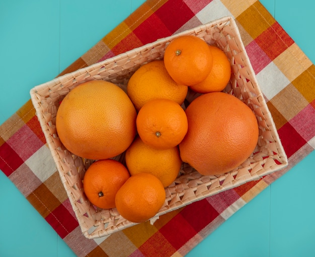 Draufsicht Orangen mit Grapefruit in einem Korb auf einem karierten Handtuch auf einem türkisfarbenen Hintergrund