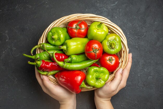 Draufsicht Paprika und Tomaten in Weidenkorbschale in weiblicher Hand auf dunkler Oberfläche