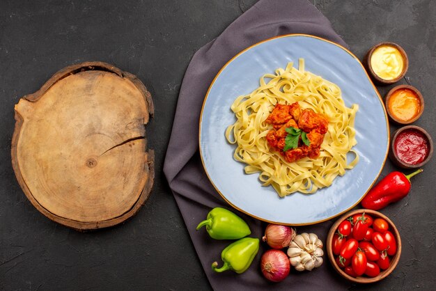 Draufsicht Pasta auf Tischdecke blauer Teller mit appetitlichen Pastaschüsseln Tomatensaucen Knoblauchzwiebelkugelpfeffer auf der lila Tischdecke und Holzbrett auf dem Tisch