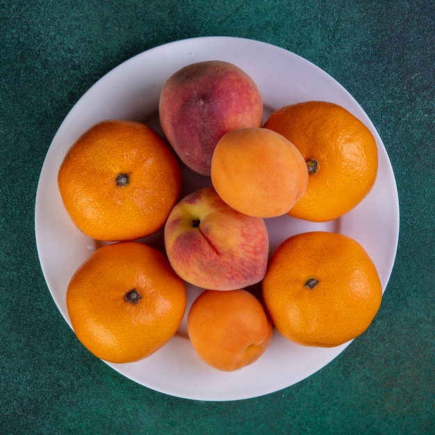 Draufsicht Pfirsiche mit Mandarinen und Aprikosen auf Teller auf Grün