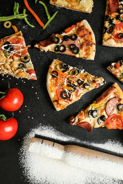 Draufsicht-Pizzamischung mit Tomatenoliven und Paprika auf schwarzem Tisch