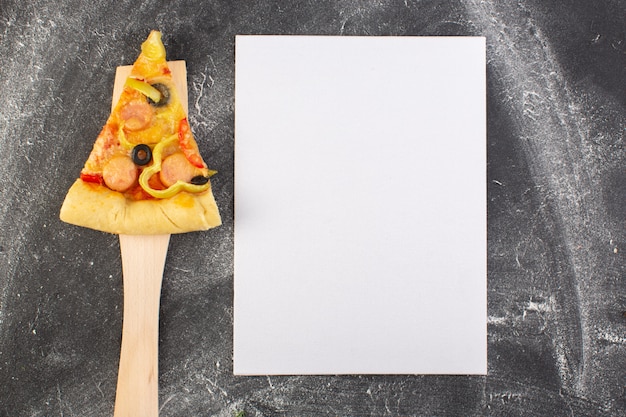 Draufsicht-pizzastück mit tomaten und würstchen der schwarzen oliven auf dem holzlöffel nahe leerem papierrohling auf der italienischen teigpizza des grauen schreibtischlebensmittels