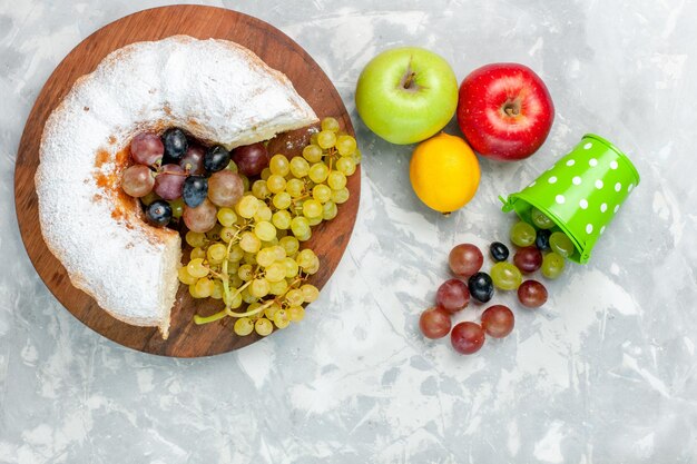 Draufsicht pulverisierter kuchen mit frischen trauben und äpfeln auf weißem schreibtisch