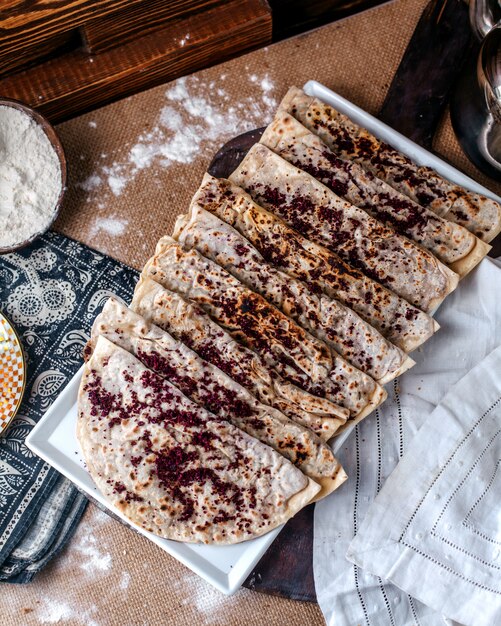 Draufsicht Qutabs berühmtes östliches Fleischmehl mit Hackfleisch im Inneren und mit braunem Gewürz namens Sumax innerhalb weißer Platte auf der braunen Oberfläche