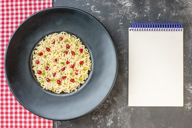 Draufsicht Ramen-Nudeln auf Teller auf rot-weiß kariertem Tischdecken-Notizbuch auf dunklem Tisch