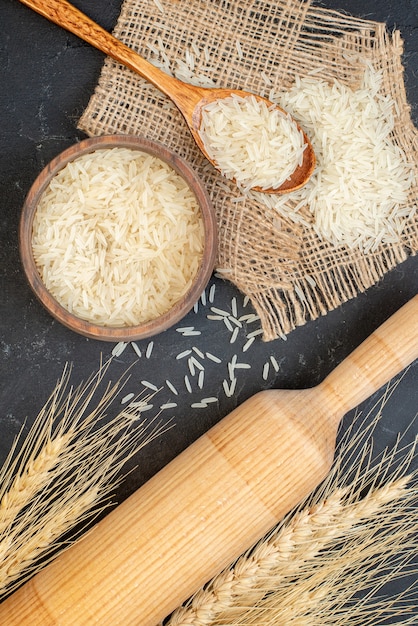Draufsicht Reis in Schüssel und Holzlöffel Nudelholz auf schwarzem Tisch